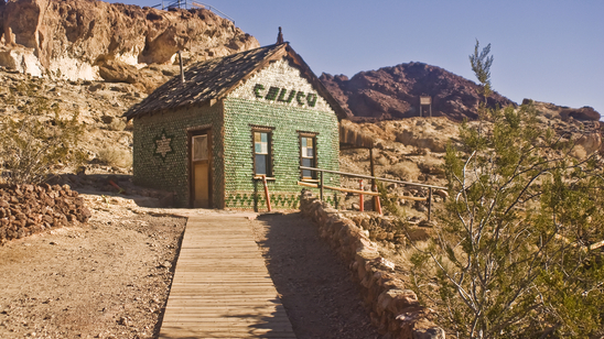 A wooden walkway leads to the famous &bottle house&, constructed entirely from bottles, in Calico, California