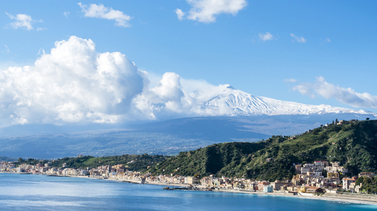 Panoramic view across the beach town of Giardini Naxos, Sicily, with snow-capped Mount Etna in the distance