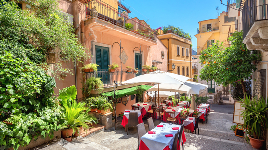 Restaurant tables set out beneath white parasols on a cobbled lane in Taormina, Sicily